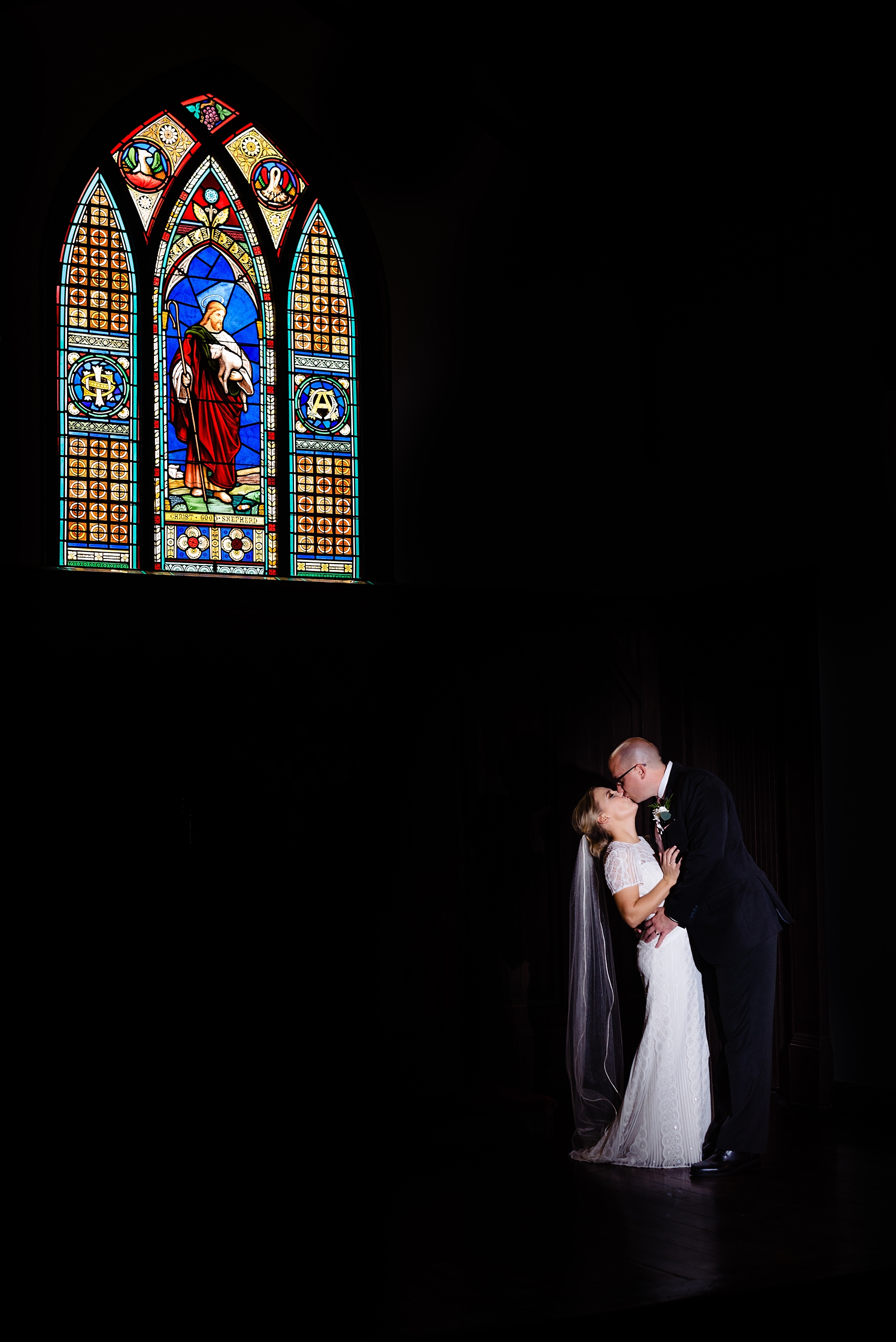 dramatic portrait of bride and groom kissing under the stained glass window at All Saints Chapel by Raleigh wedding photographers