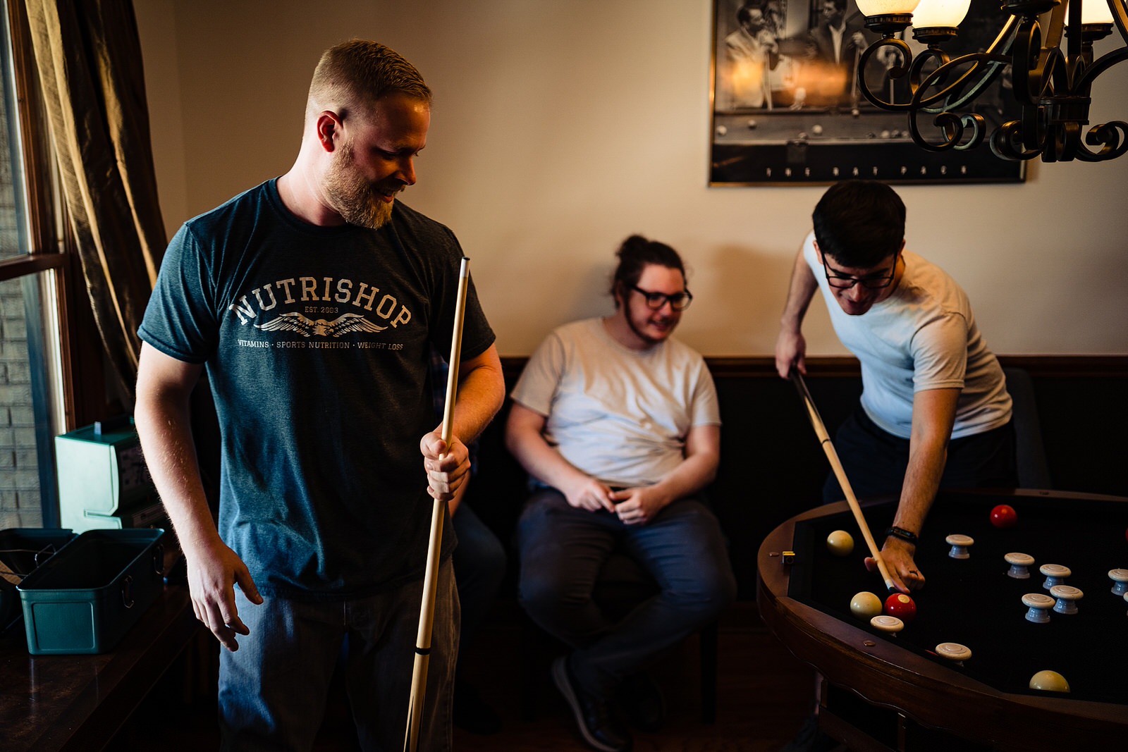 Groomsmen play pool before getting ready for The Meadows Raleigh wedding ceremony