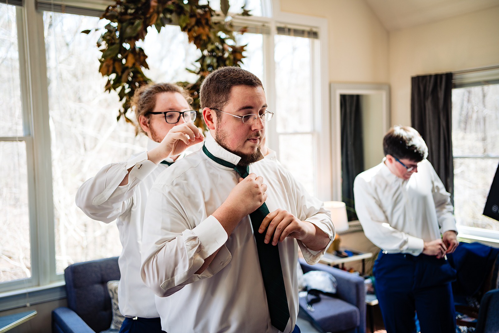 Groom's brother helps him put on his tie by Raleigh wedding photographers