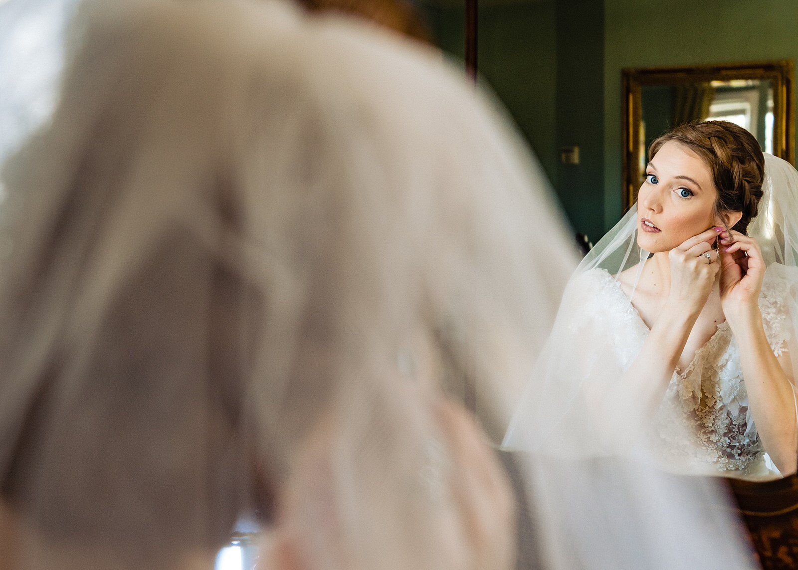 Bride looks into mirror to put on her earrings on her wedding day, by Raleigh wedding photographers