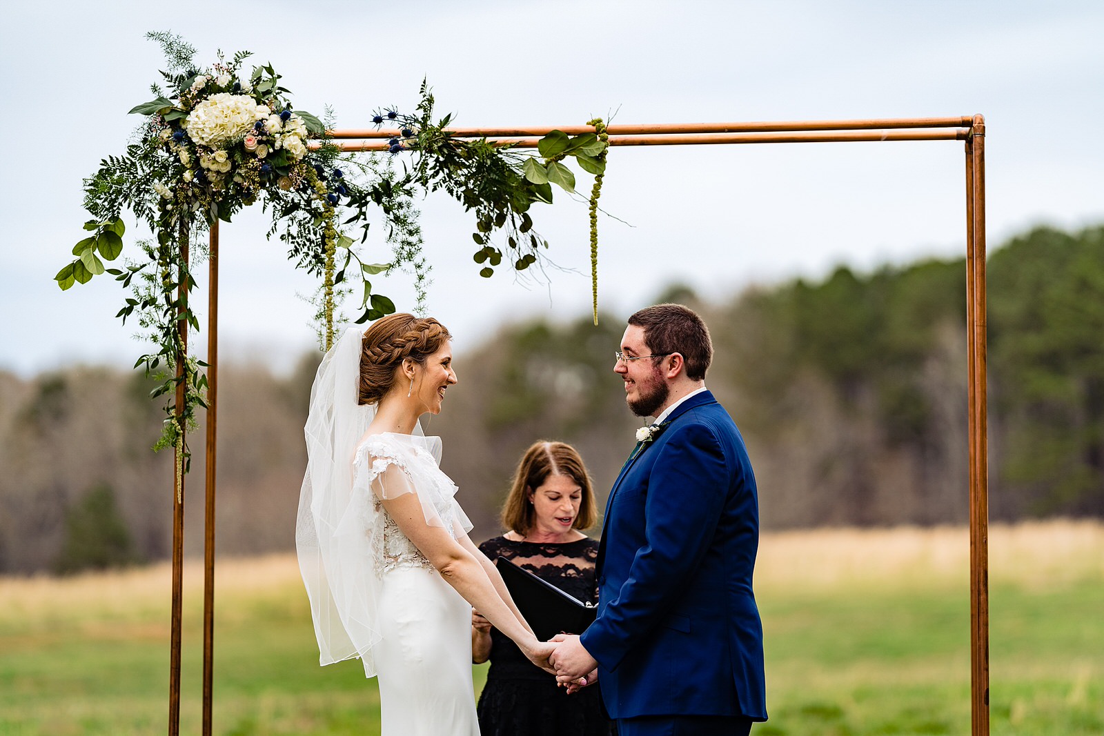 Bride and groom stand under a copper arbor during their ceremony at The Meadows Raleigh