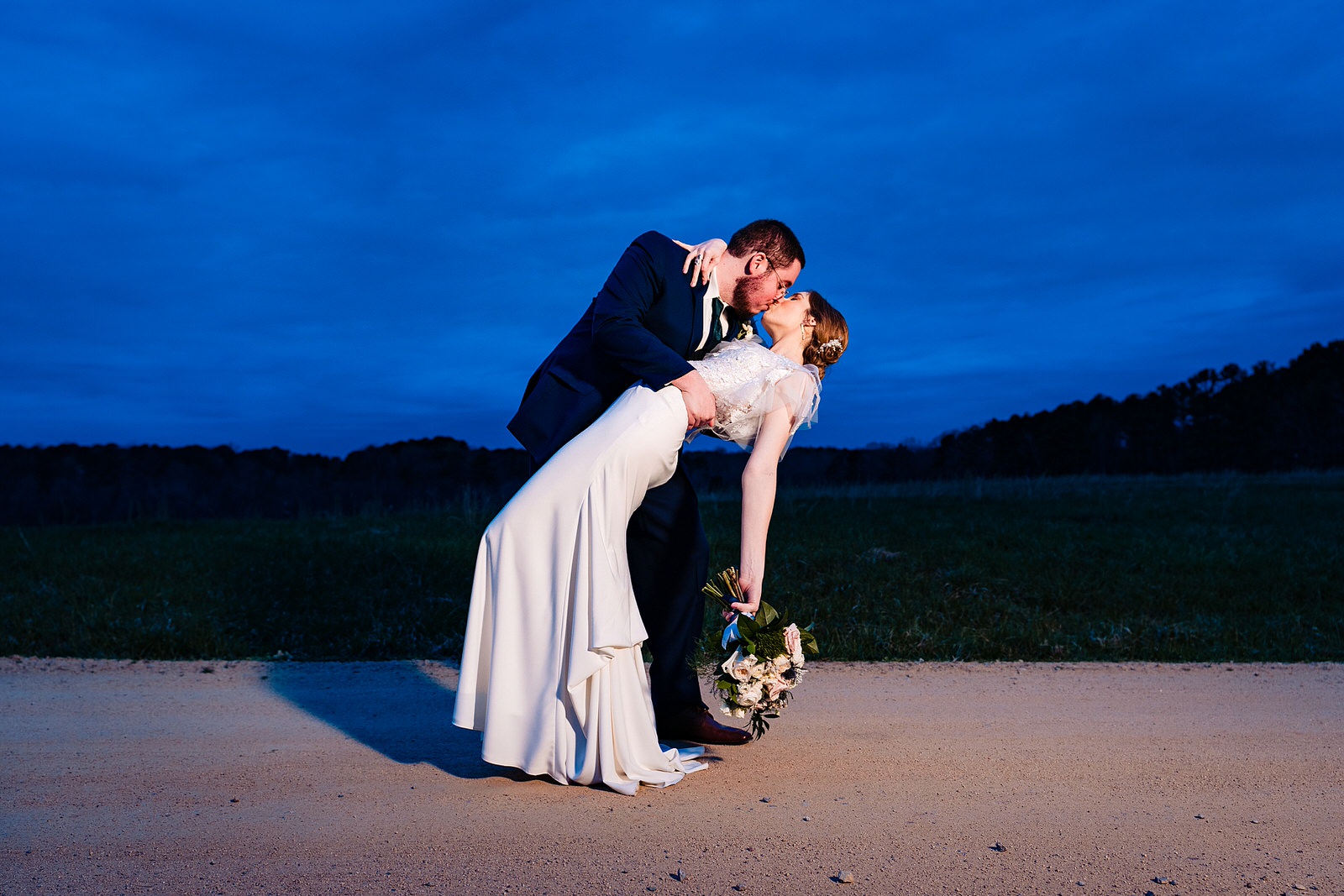 Groom dips Bride in front of a deep blue sky at The Meadows Raleigh