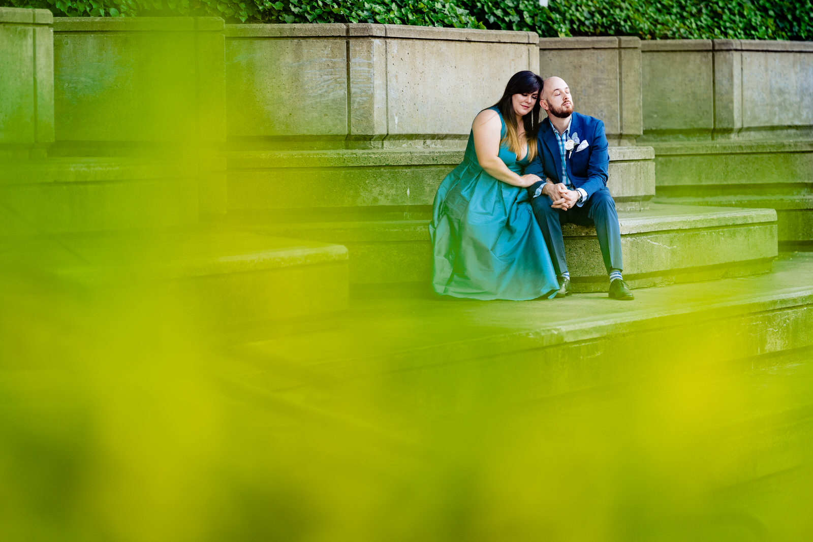Portrait of a man and a woman leaning on one another, shot through green leaves