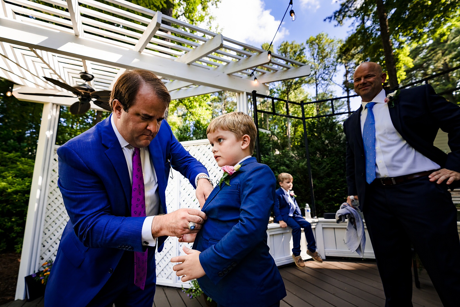 Friend of the groom helps the groom's son get buttoned into his suit coat