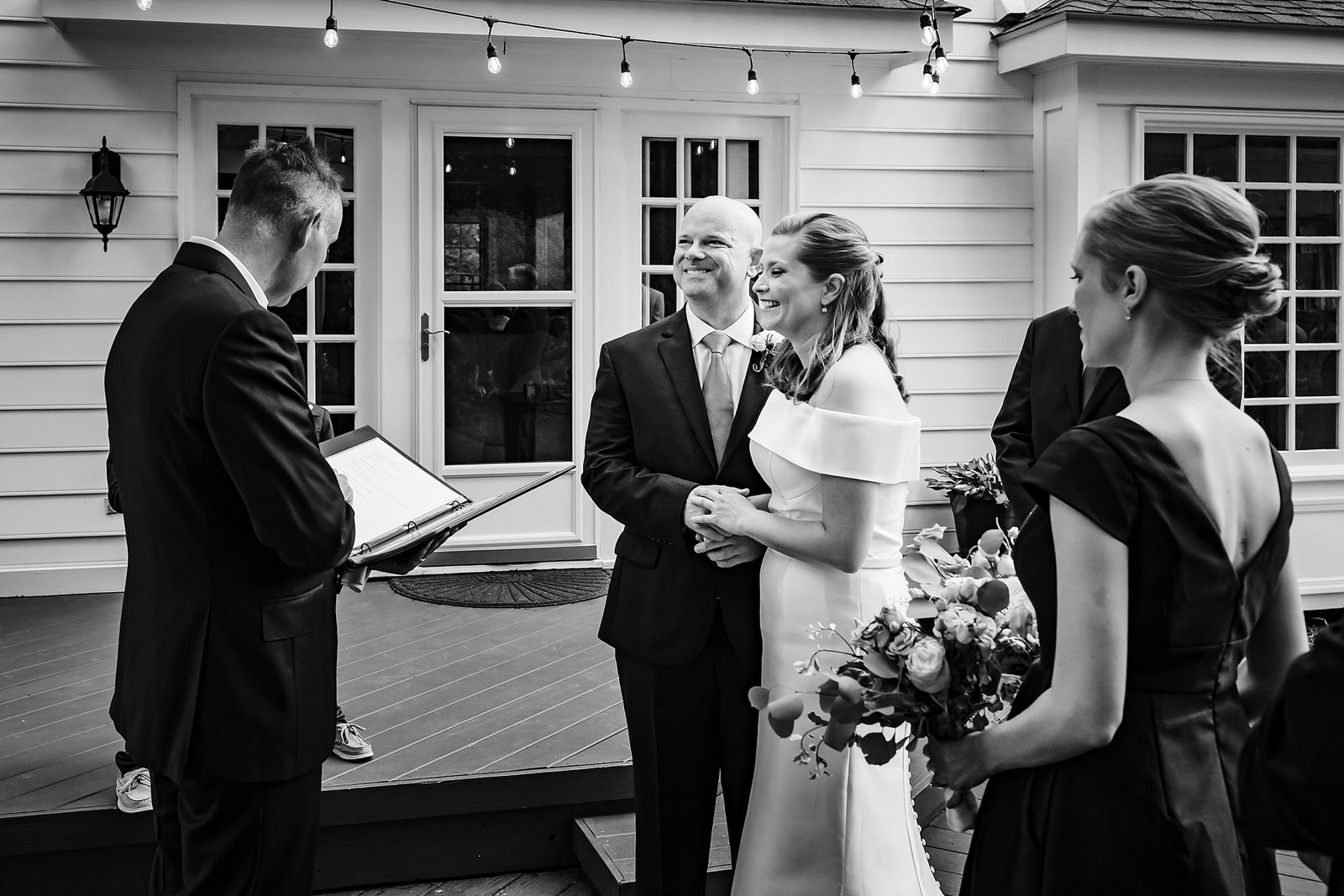 Black and white image of a bride and groom holding hands and smiling during their Raleigh backyard wedding ceremony