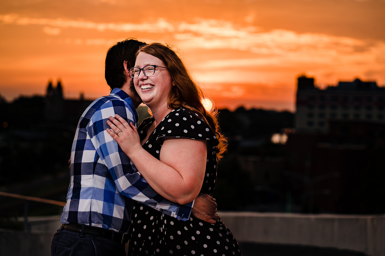 A couple embraces in front of the backdrop of an orange sunset