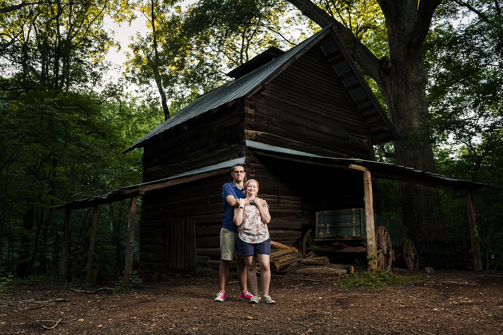 An engaged couple stands in front of one of the buildings at the West Point on the Eno park