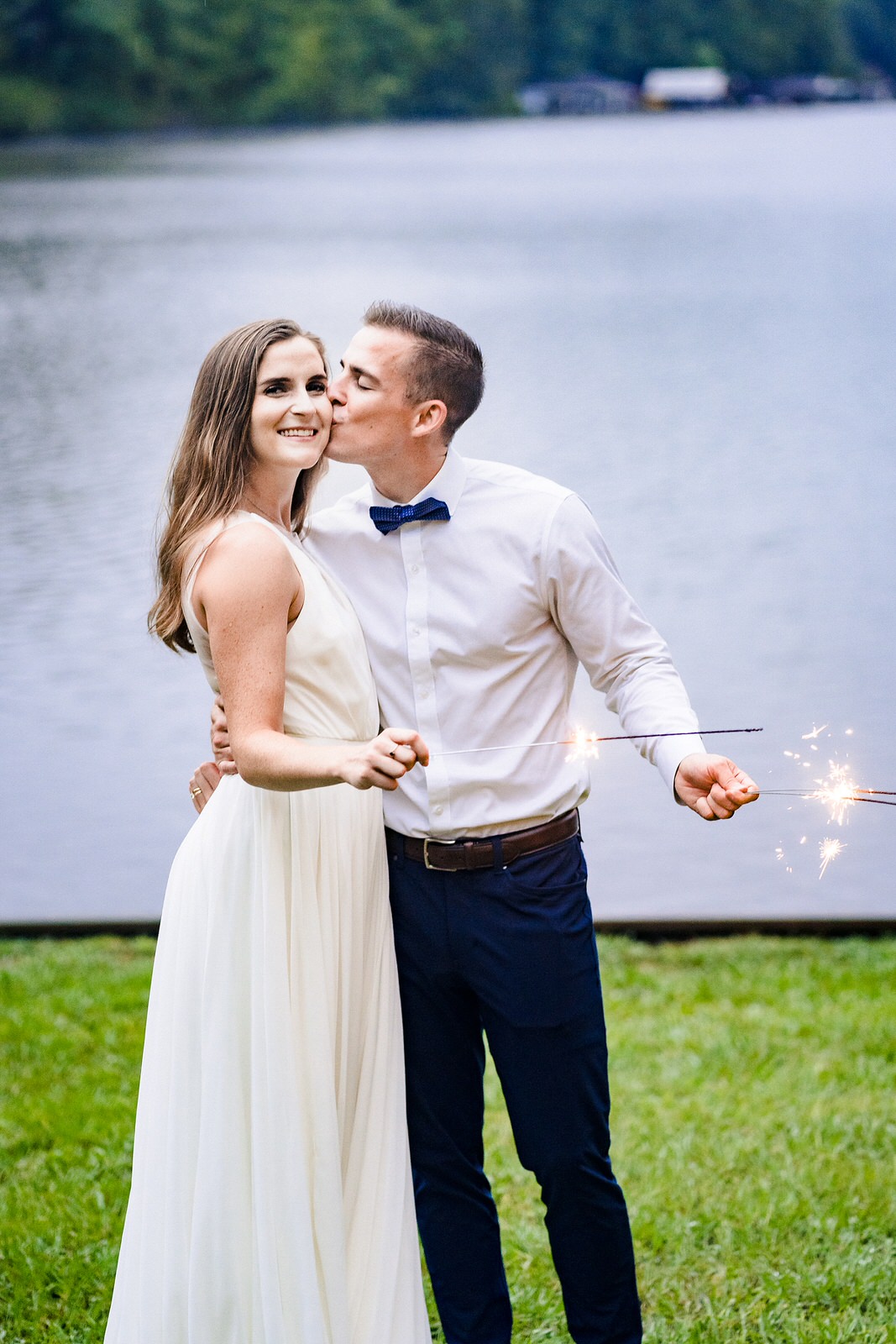 Bride and groom pose with sparklers in front of a lake
