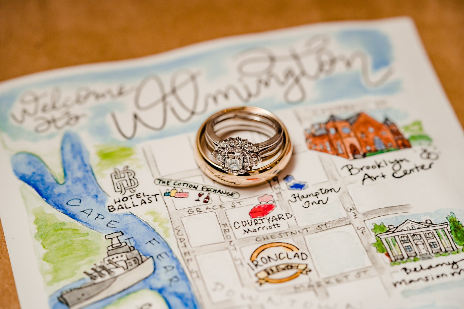 A couple's wedding ring set sits on top of a hand drawn map of Wilmington, NC featuring their hotels, their wedding venue, the Brooklyn Arts Center, and several local attractions