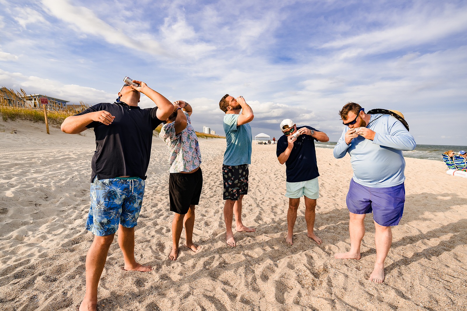 Groom and his friends shotgun beers at a casual beach wedding reception