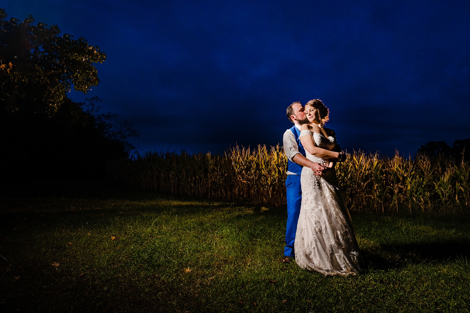 Bride and groom pose for a dramatic portrait at blue hour in a cornfield at their farm wedding
