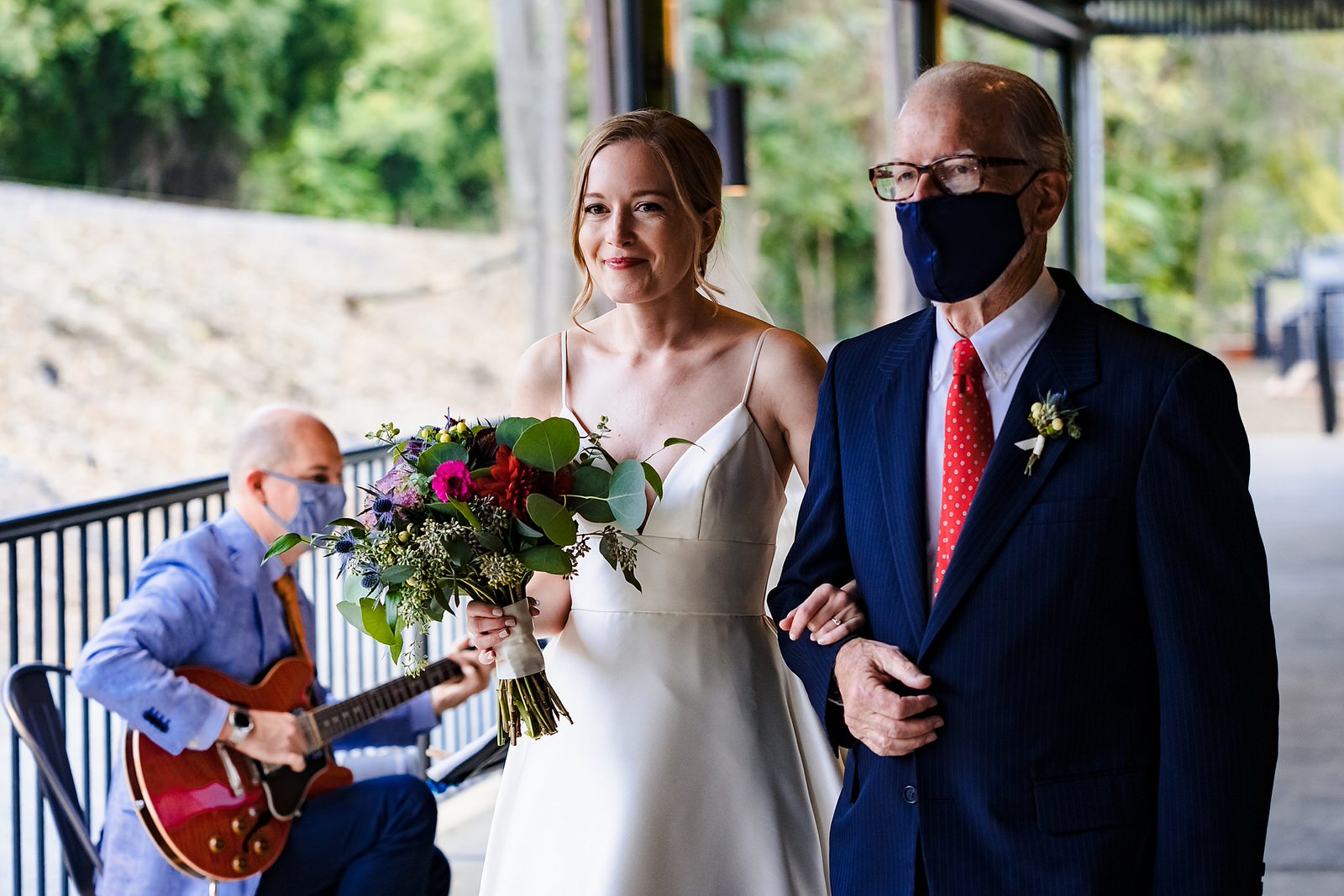 Father of the bride wears a mask as he walks her down the aisle