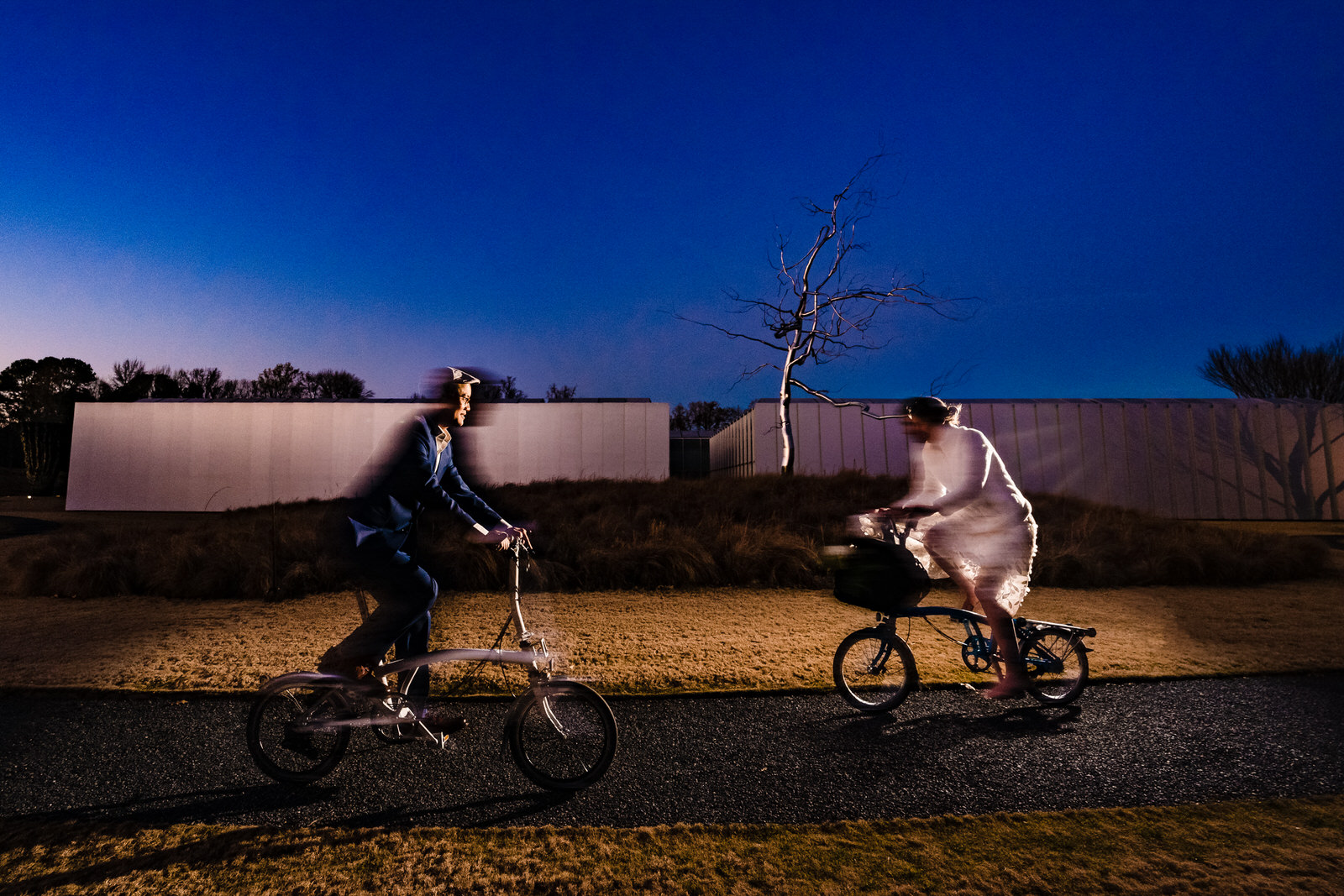 bride and groom ride through the North Carolina Museum of Art on their bicycles after their winter elopement