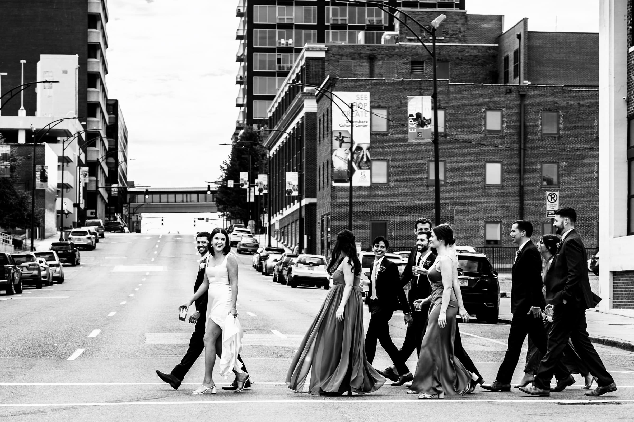 a couple in wedding attire and their wedding party walks down the street in Greensboro, NC | photos by Kivus & Camera