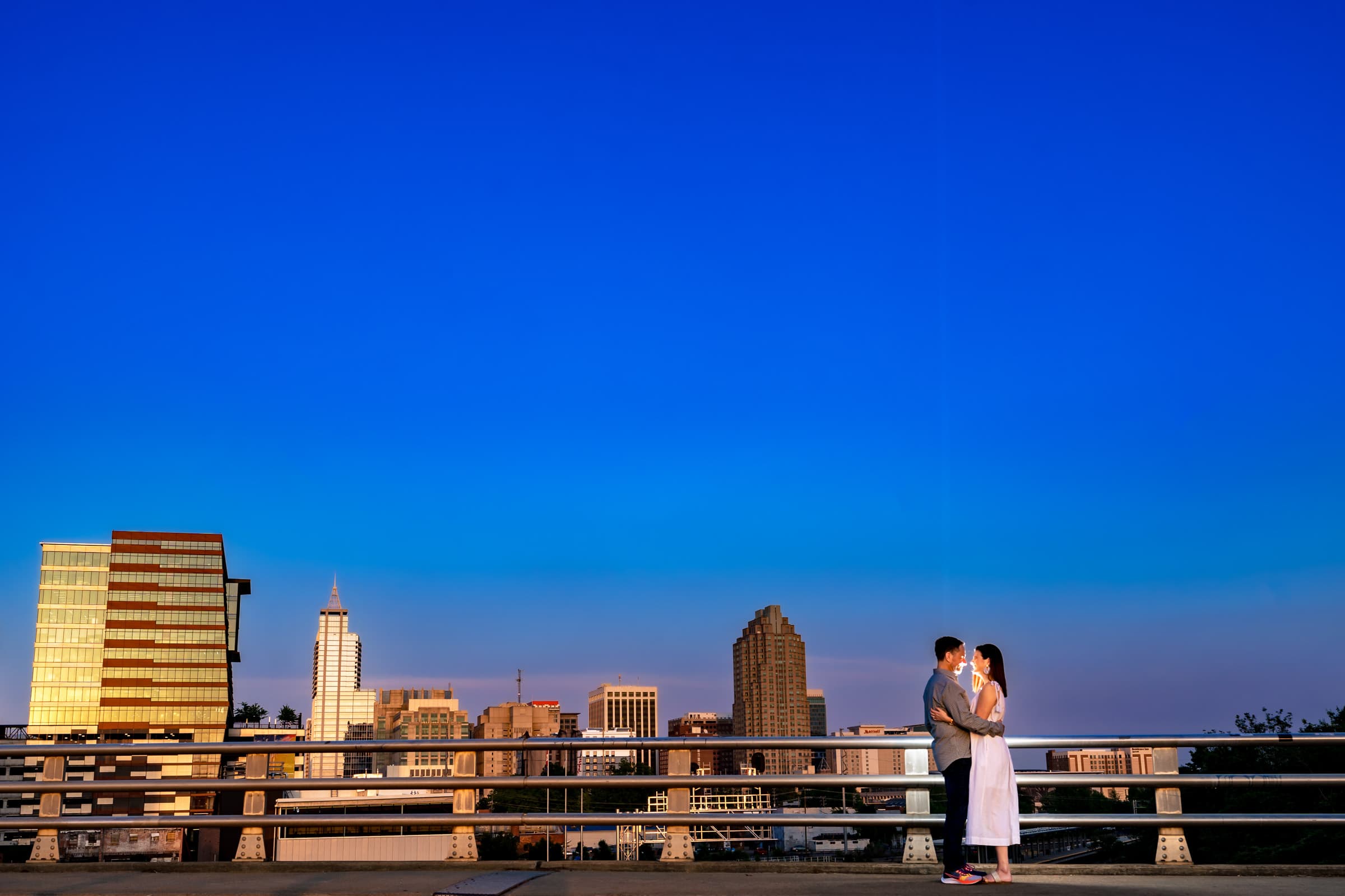 portrait of an engaged couple with the Raleigh skyline in the background behind them | photo by Kivus & Camera
