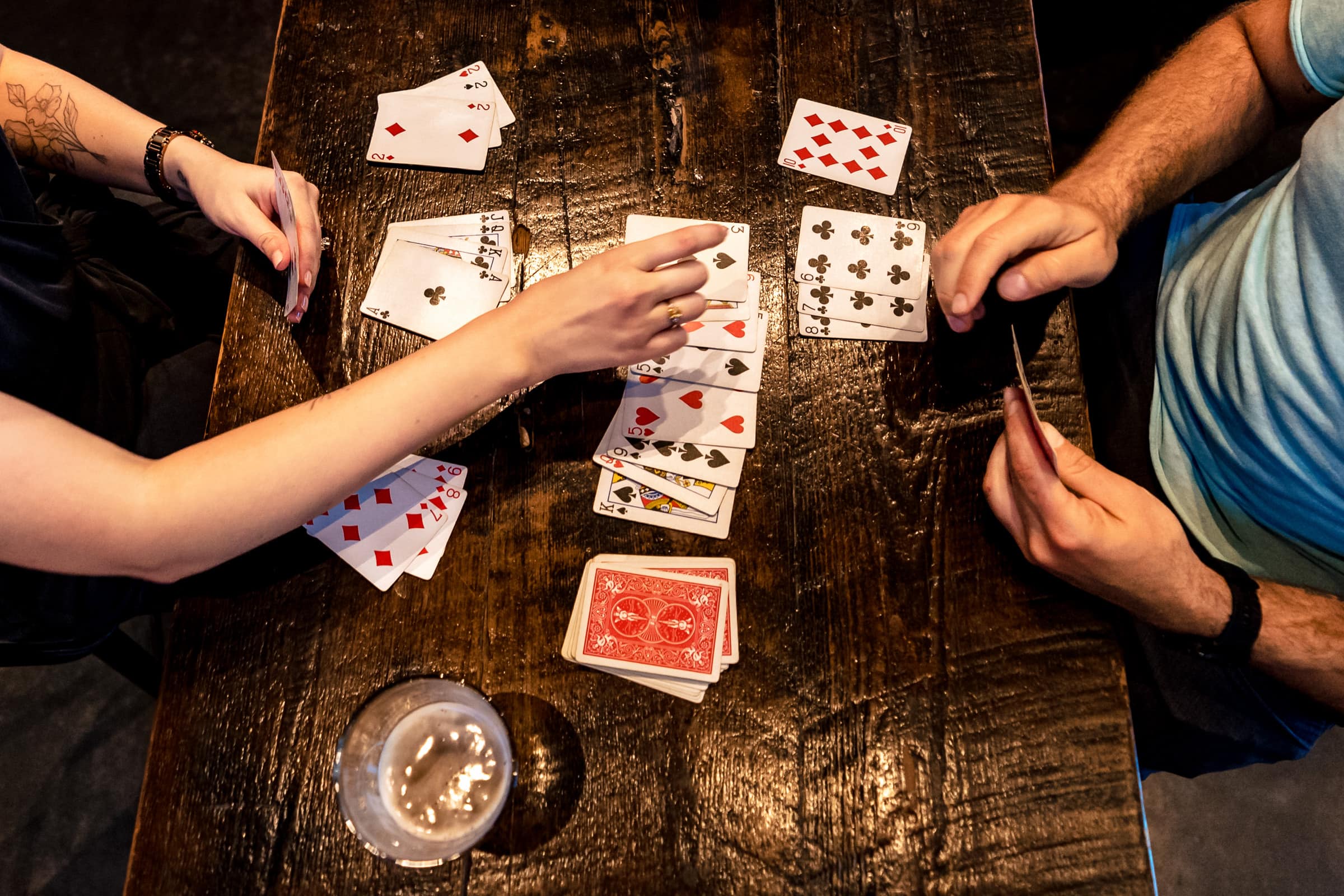 overhead photo of playing cards on a table, with two pairs of hands coming in to move the cards around