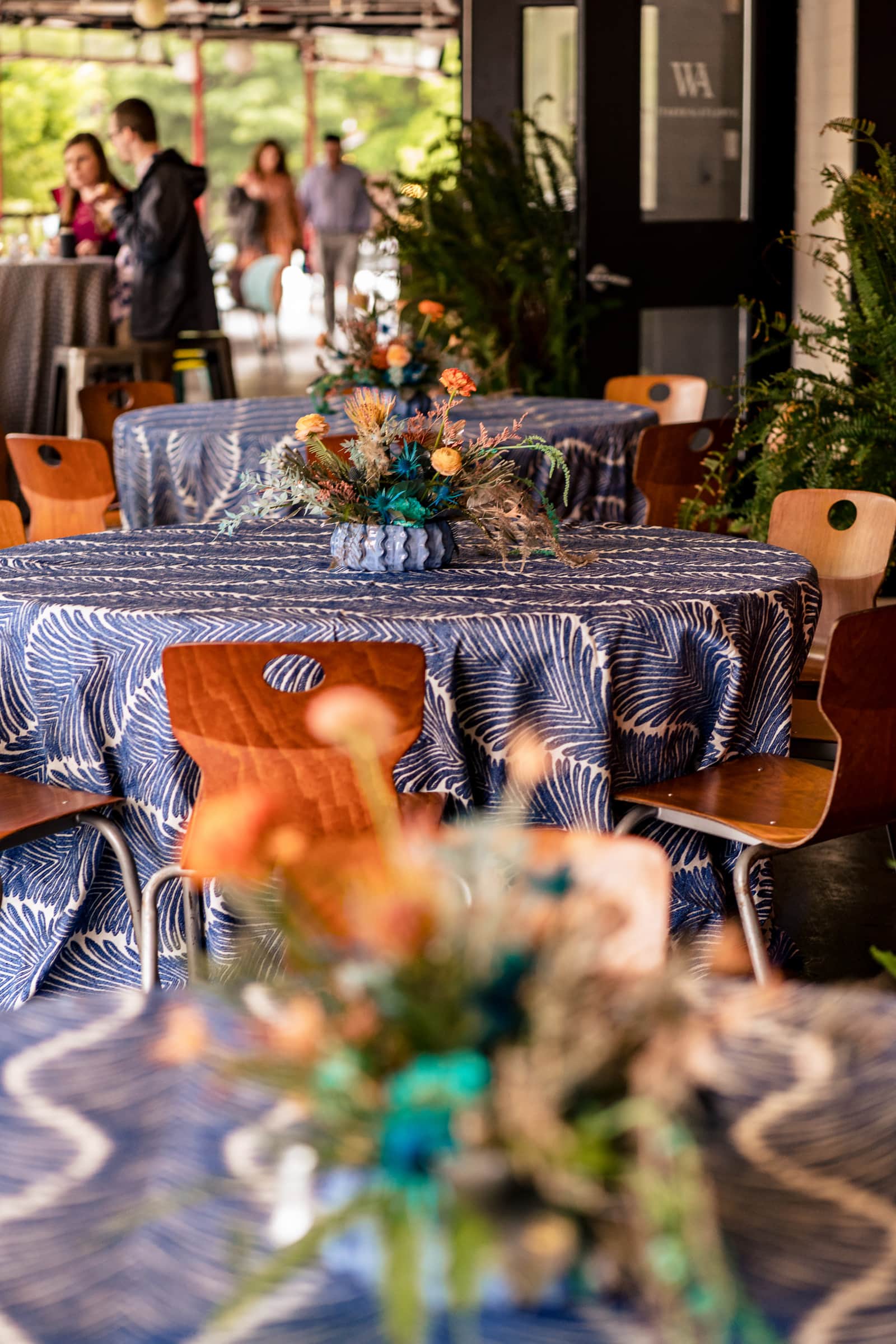 tables on the deck at Whitaker & Atlantic wedding are decorated with blue and white table cloths and yellow and orange florals | photo by Kivus & Camera