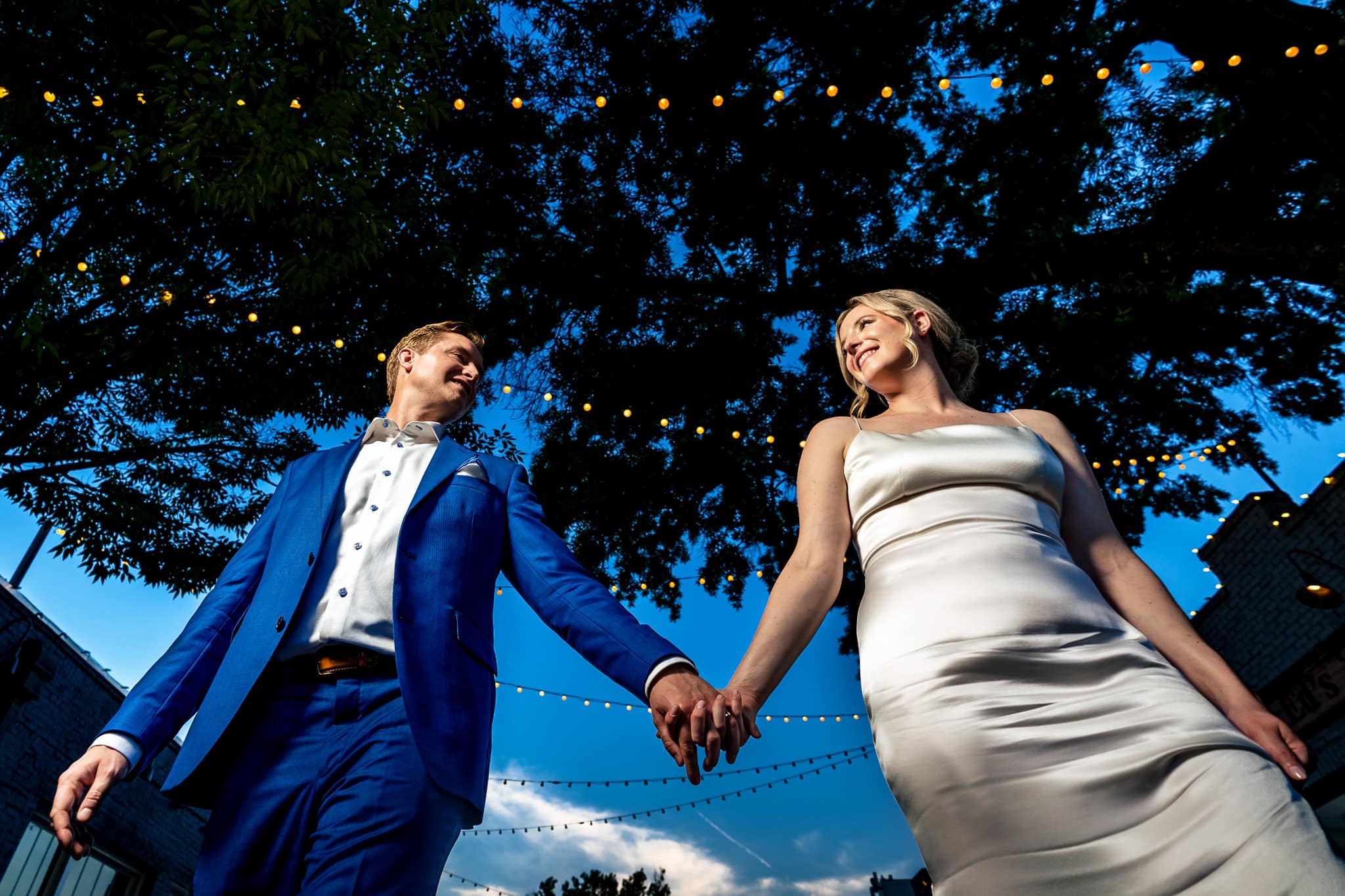 bride and groom holding hands and looking at each other with a blue sky background at The Grove at City Market