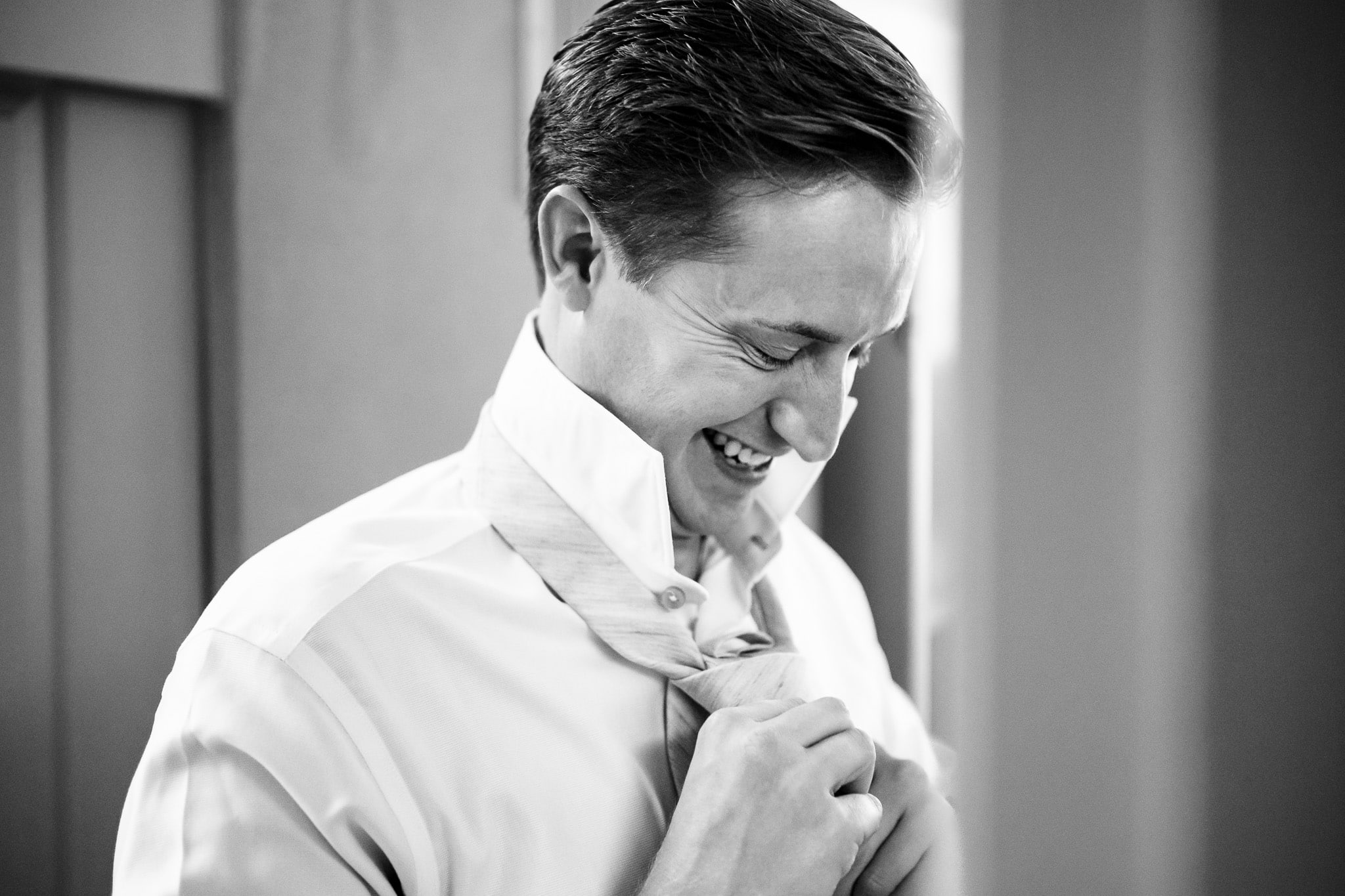 groom laughs as he ties his tie | photo by Kivus & Camera