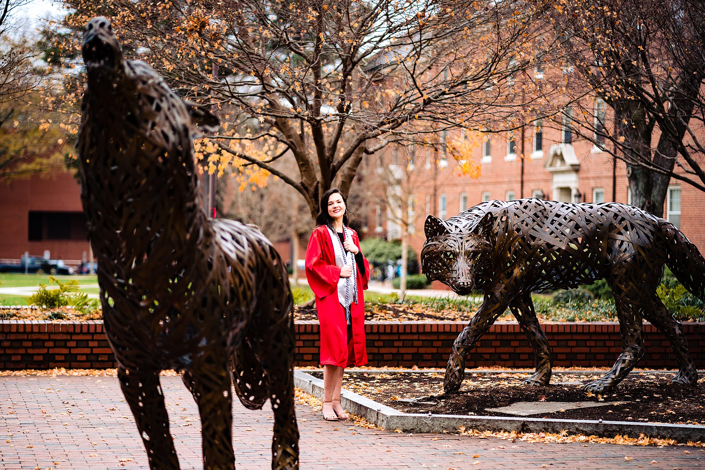 An NC State Graduate poses in her red graduation robe for senior portraits in Wolf Plaza at NC State's Raleigh, North Carolina campus | kivusandcamera.com