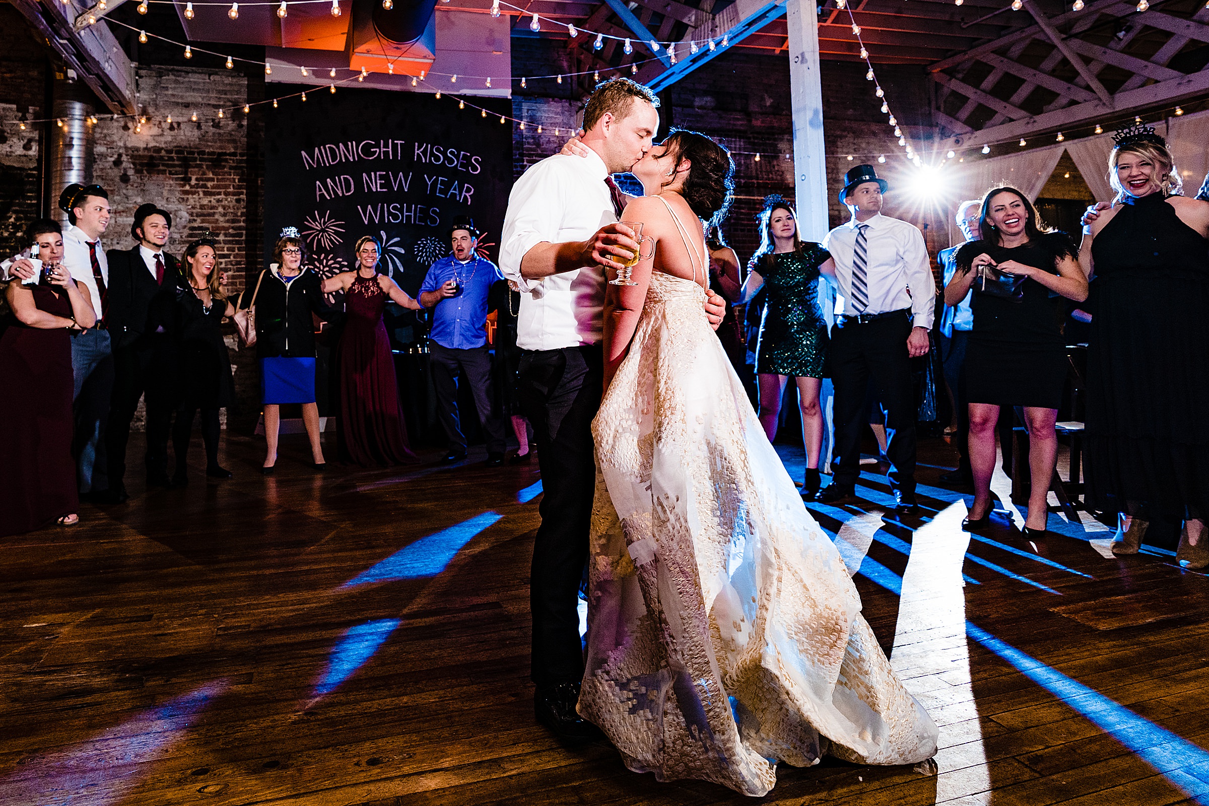 Bride and groom kiss at midnight during their New Year's Eve wedding at the Stockroom in Raleigh, North Carolina. The bride is in a white and gold dress, and the groom is in a suit but has taken his jacket off. | kivusandcamera.com