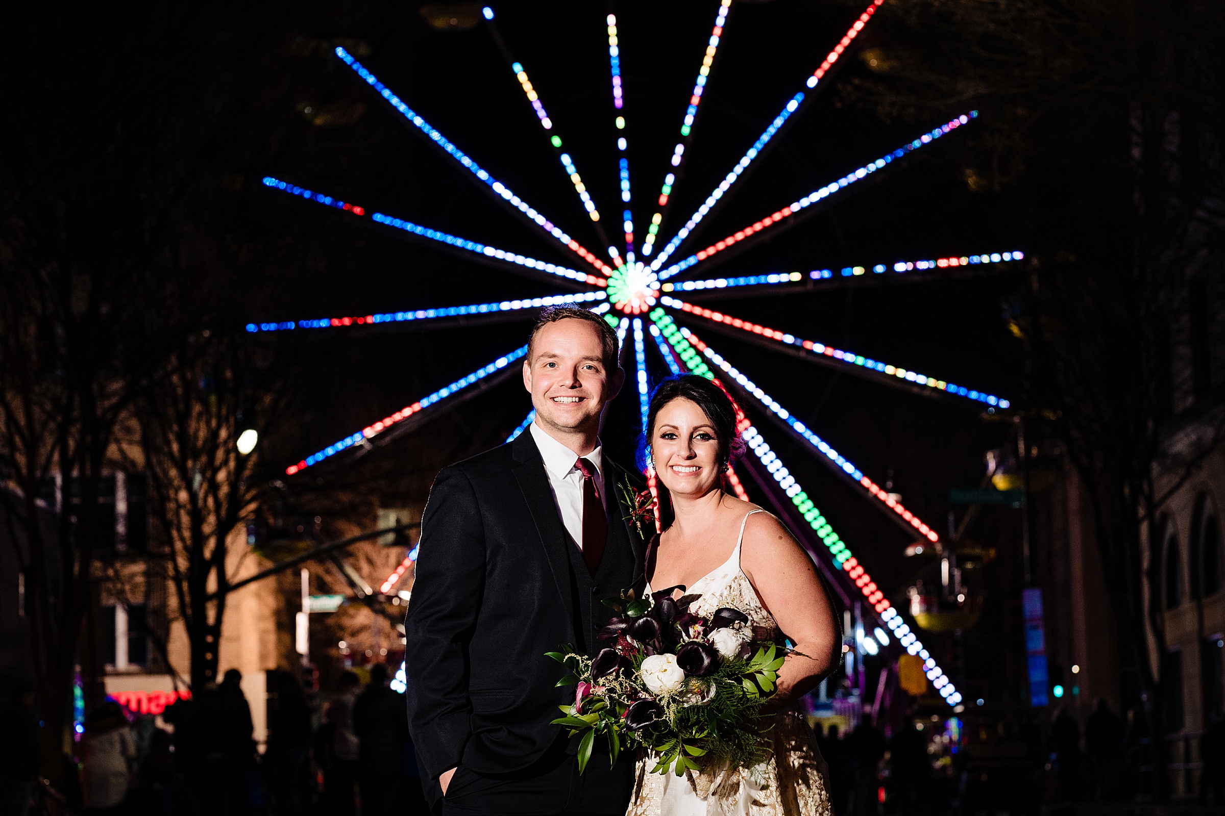 A bride and groom smile in front of a lit up ferris wheel in downtown Raleigh on New Year's Eve | kivusandcamera.com