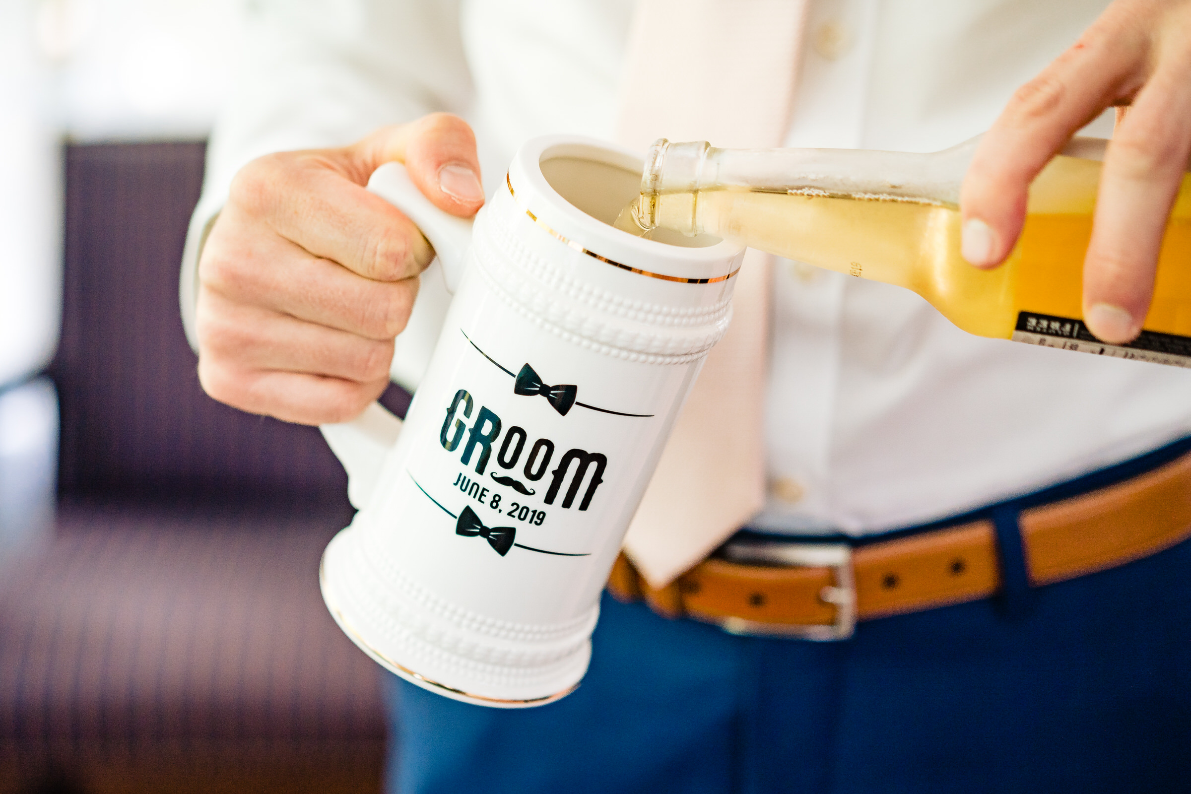 detail shot of a man in a suit pouring a beer into a custom beer stein that says Groom by Raleigh wedding photographers