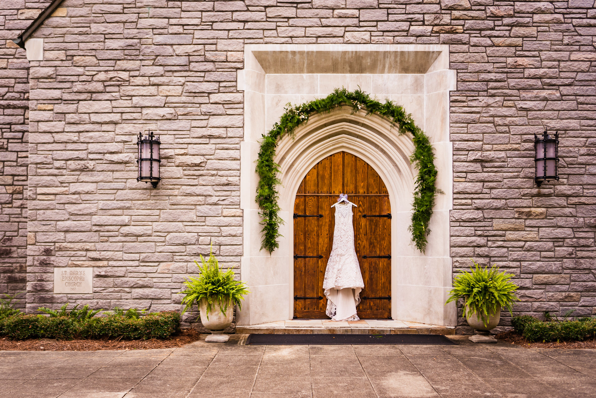 A white wedding gown hangs in the center of a wooden door for a stone church outside of Raleigh, North Carolina