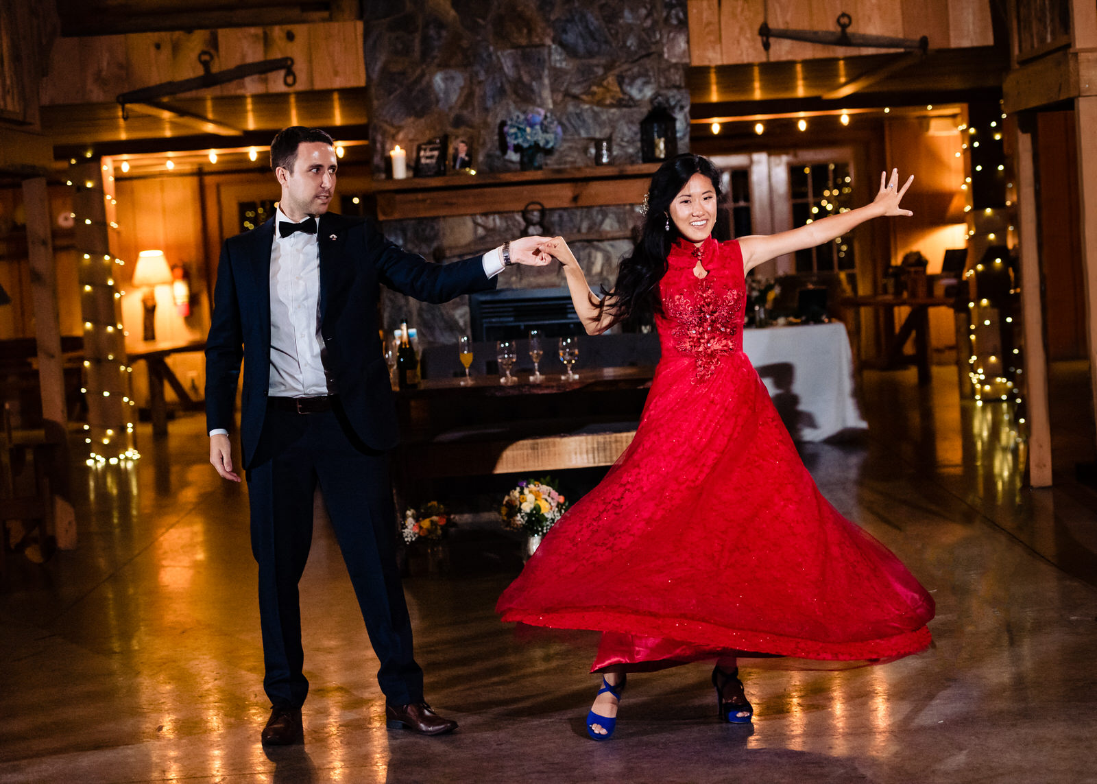 Groom in a tuxedo twirls a bride in a red wedding dress