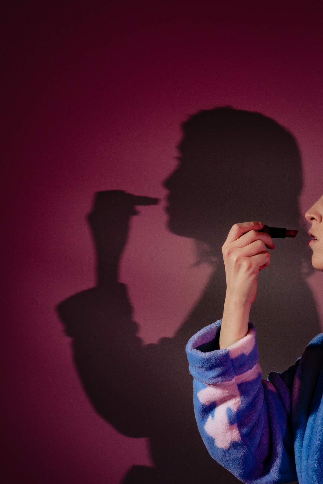bride puts on lipstick with her shadow projected onto a pink wall