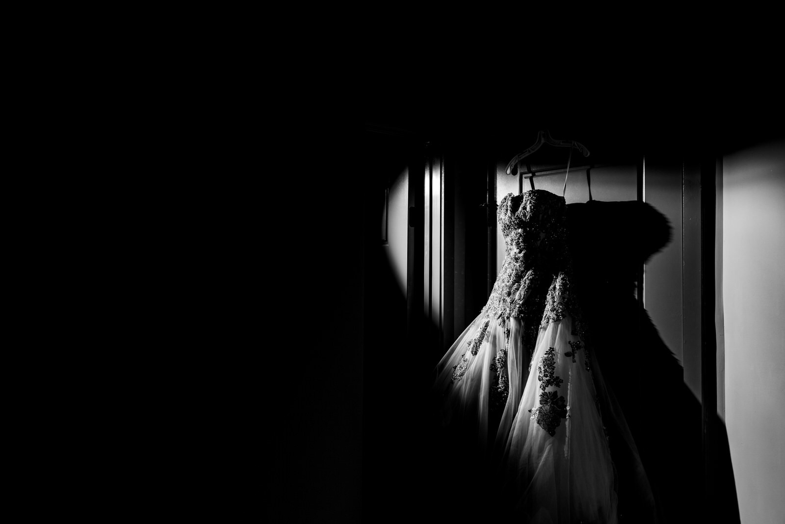 Wedding dress hangs on a door with a shaft of light illuminating it. Part of the quarantine wedding project