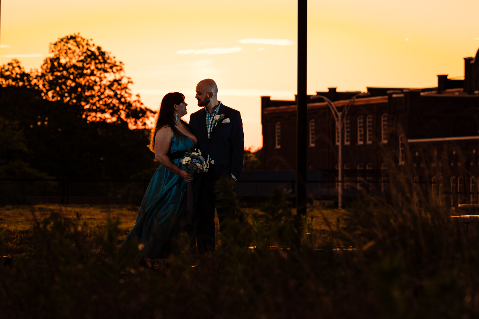 Couple poses in front of an orange sunset during a Durham anniversary portrait session