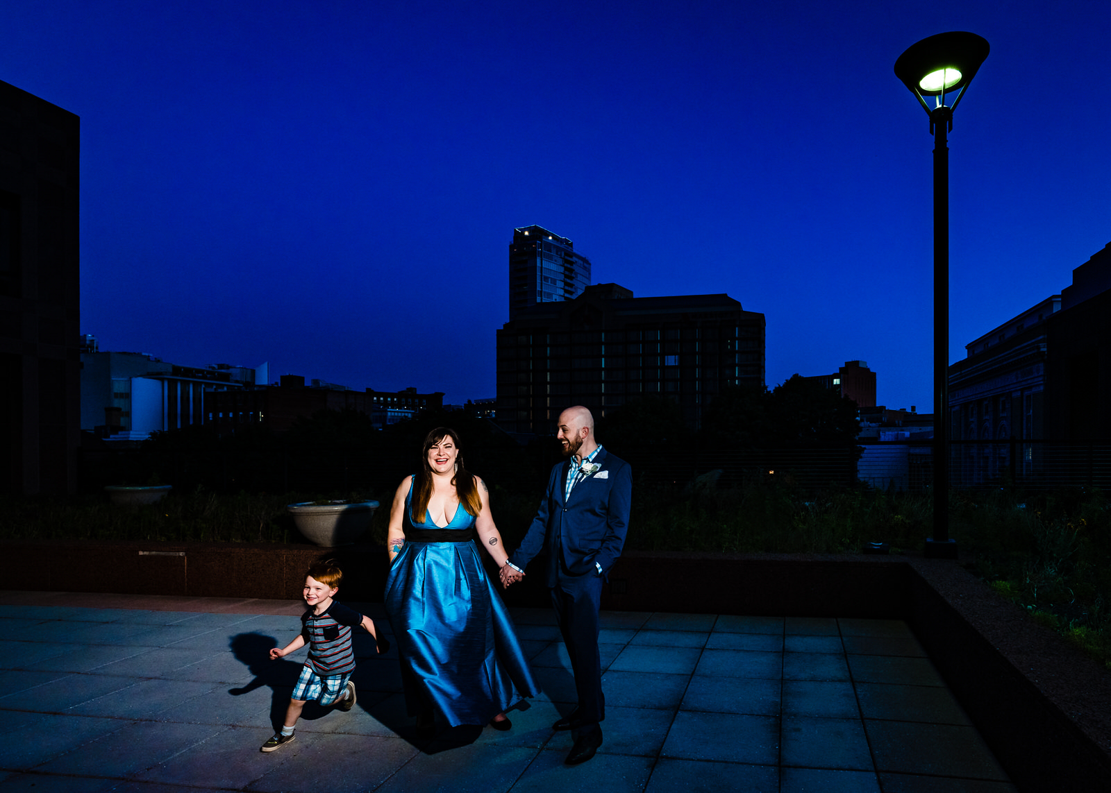 Dramatic night portrait of a husband and wife with their young son running by them