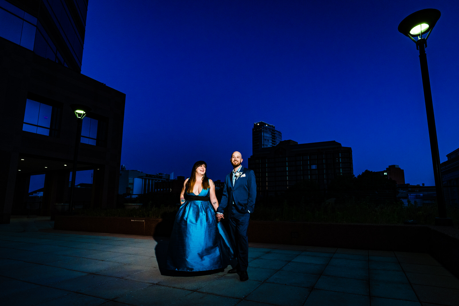 Couple poses for portrait with the downtown Durham skyline and a deep blue sky behind them