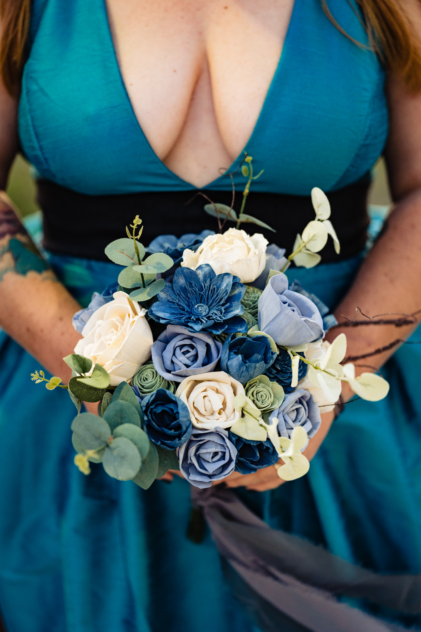 Closeup of a blue and white wood flower bouquet held by a woman in a teal dress