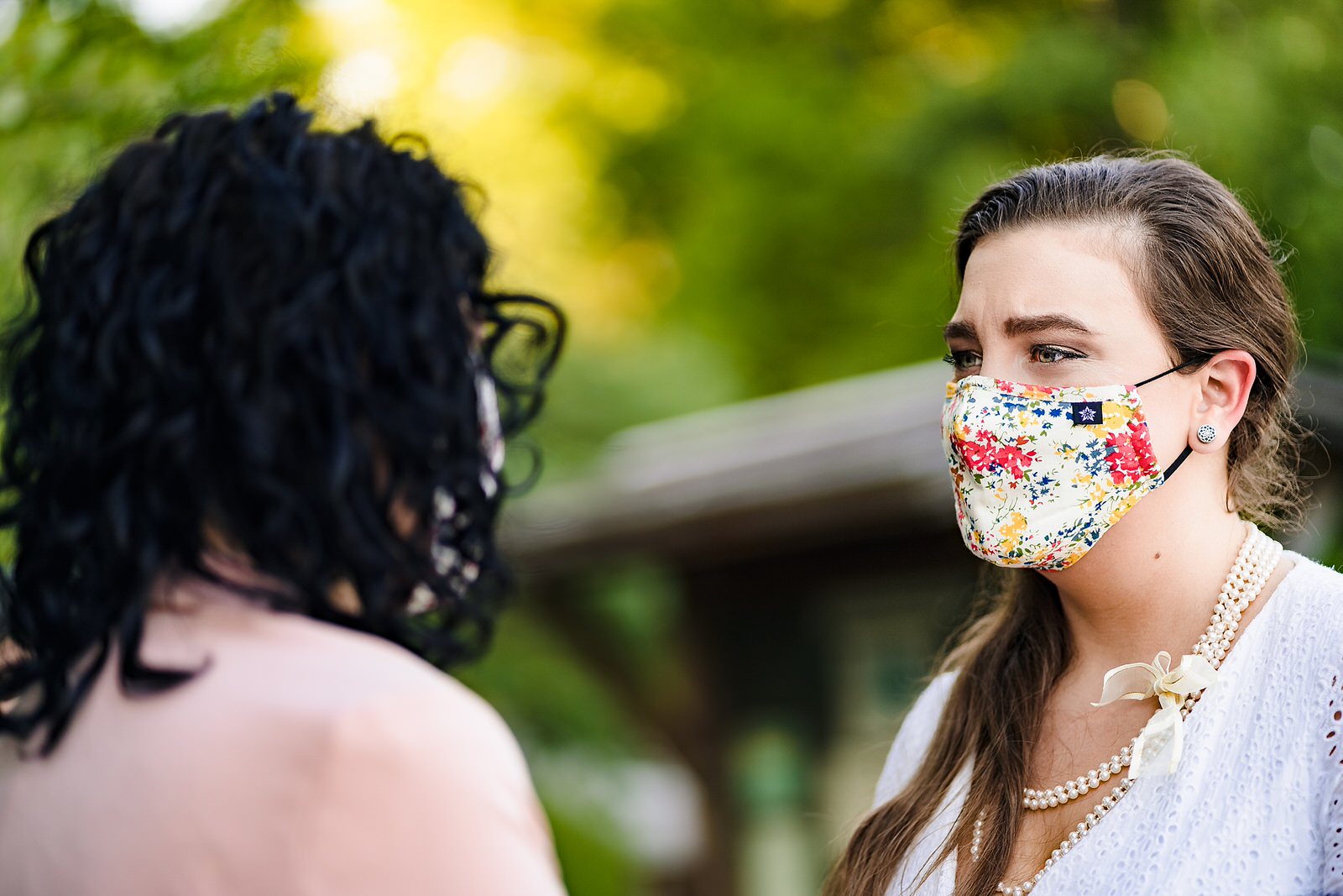A bride in a mask tears up as she looks at her partner during their same-sex elopement