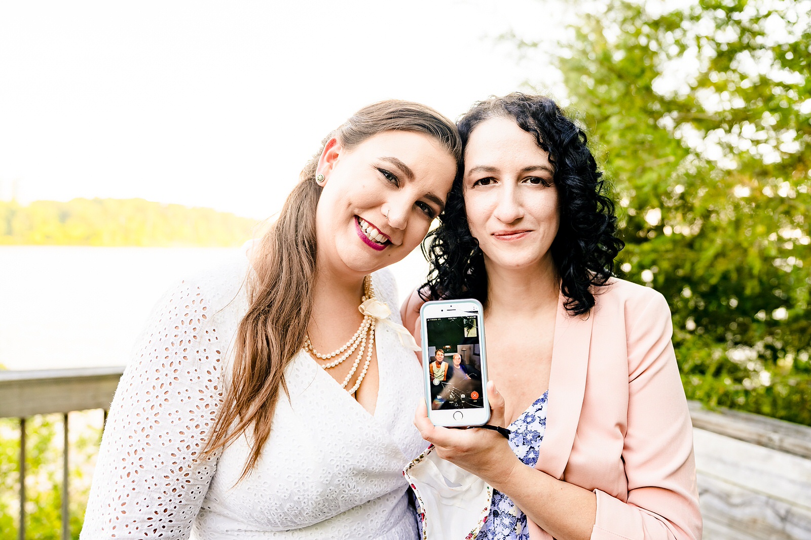 Two brides pose with one bride's parents who have facetimed in to the wedding ceremony