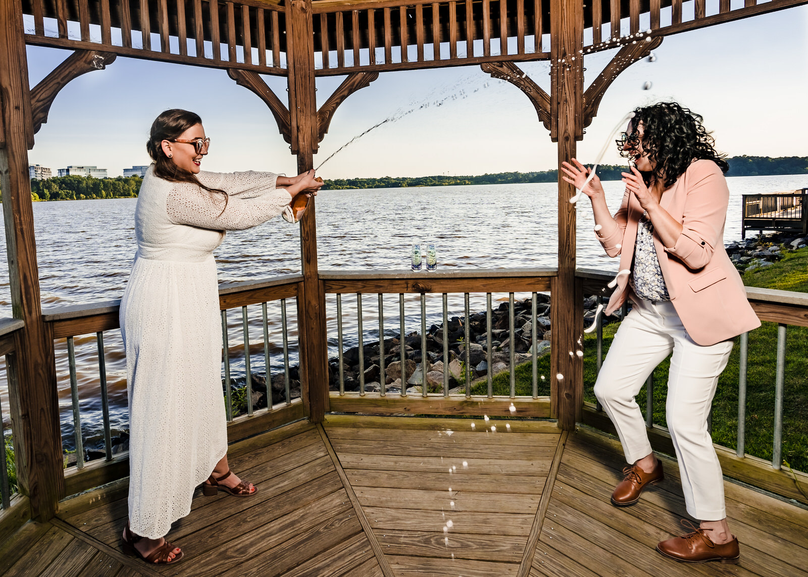 A woman pops champagne right after an intimate Raleigh elopement. Her new wife jumps to get out of the spray.