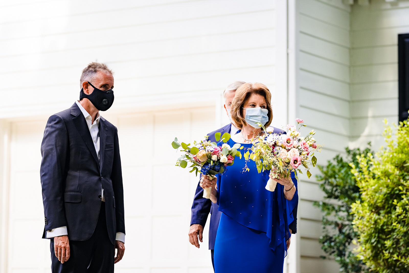 Mother of the bride, wearing a face mask, holding bouquets