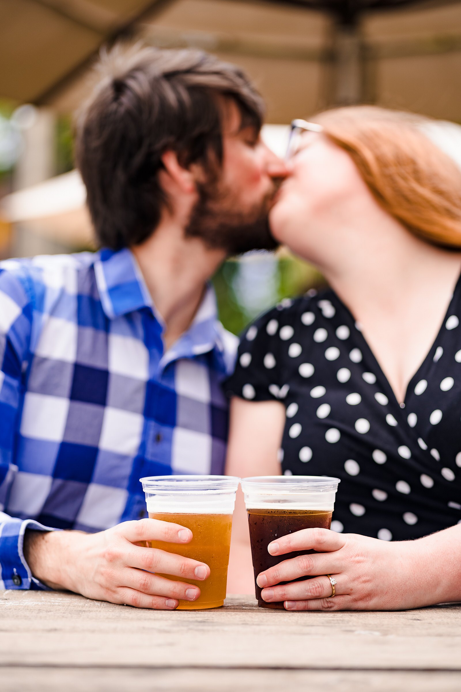 An engaged couple kisses while holding beers at Durham brewery Ponysaurus for their engagement photos