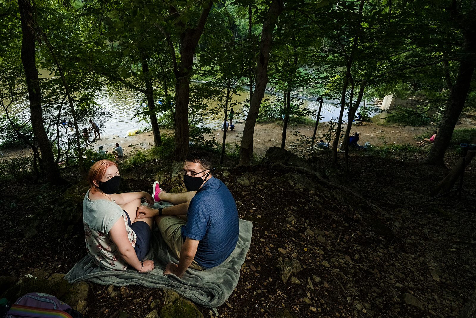 Engaged couple wearing masks due to Covid, sit in front of the Eno River