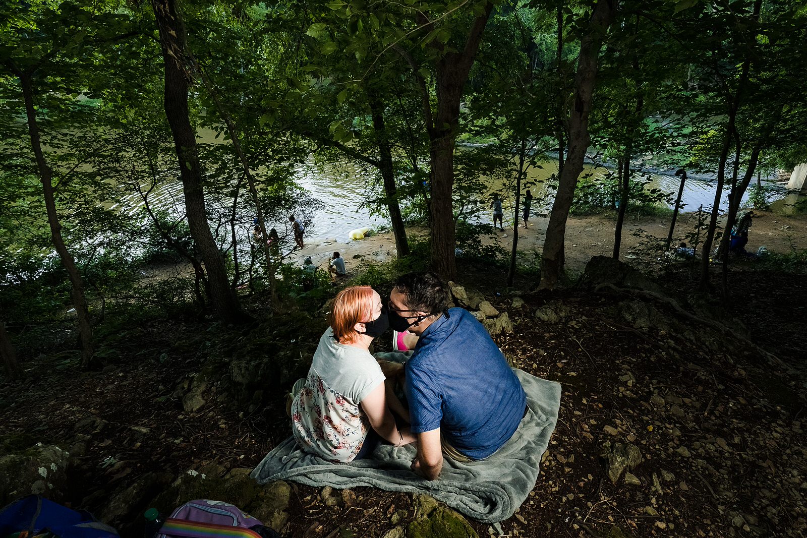 Engaged couple wearing masks due to Covid, kiss in front of the Eno River