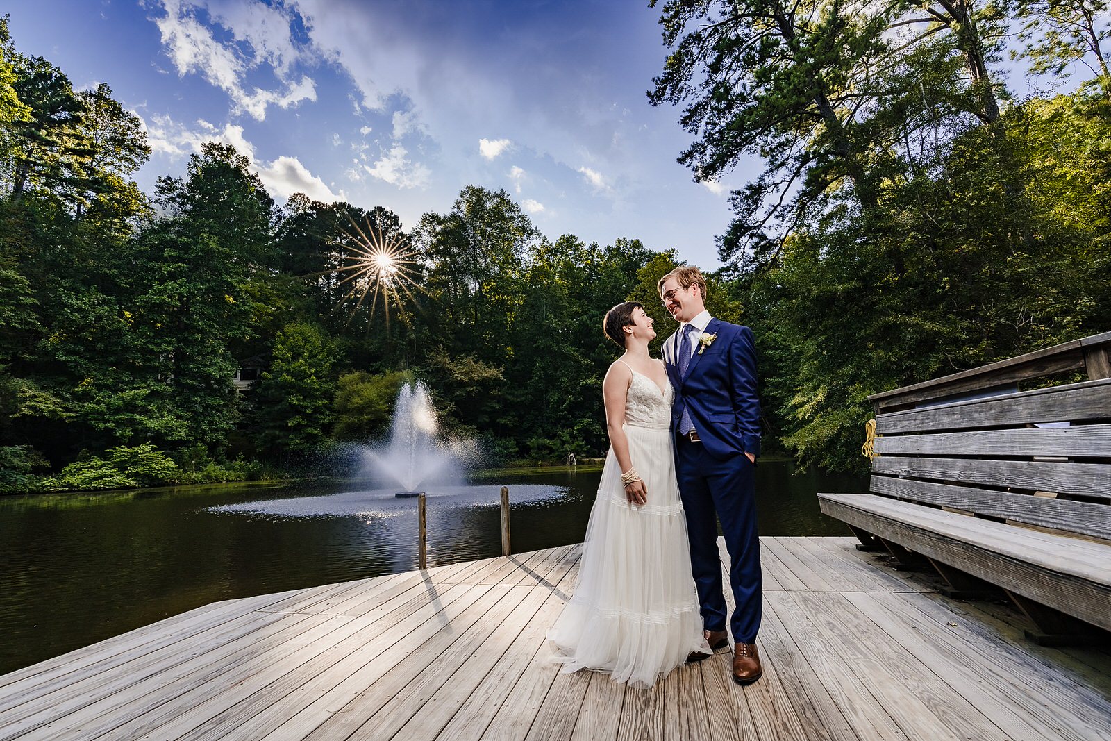 Bride and groom hug in front of a lake with a fountain