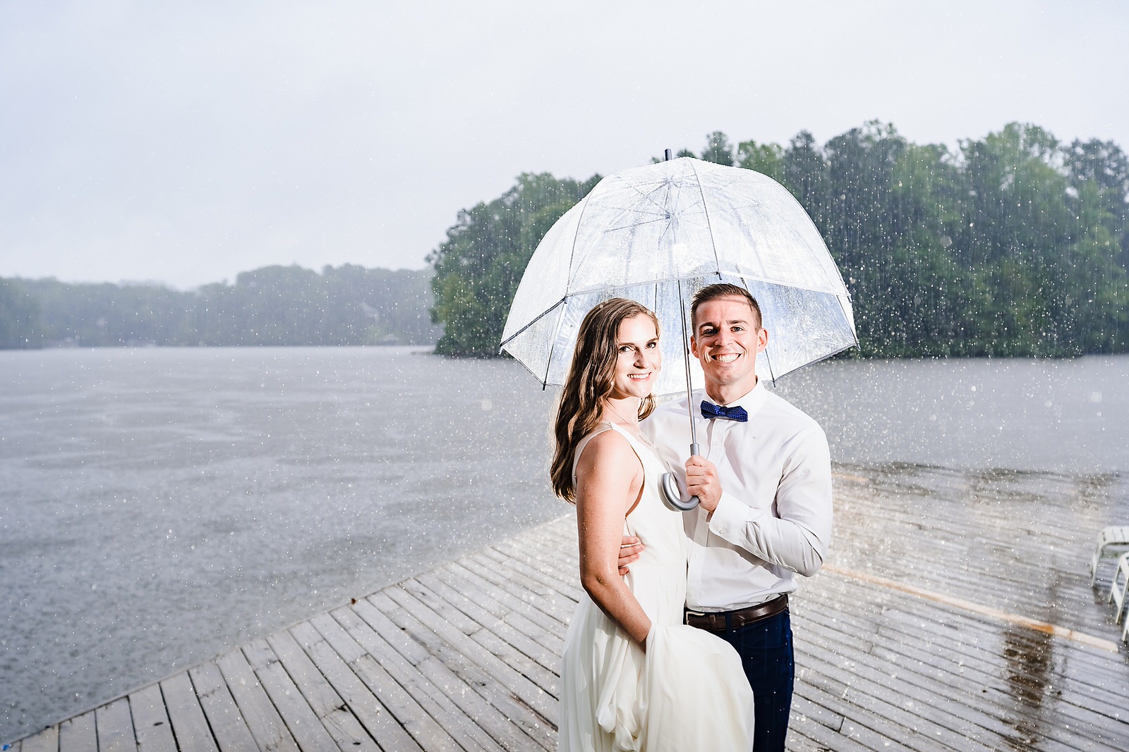 Bride and groom smile under an umbrella in the pouring rain
