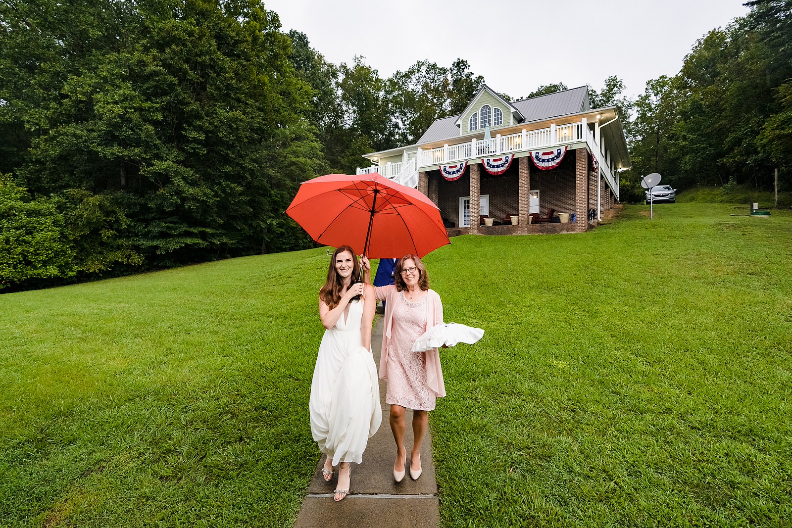 bride walks to ceremony location with her mother; both are under an umbrella