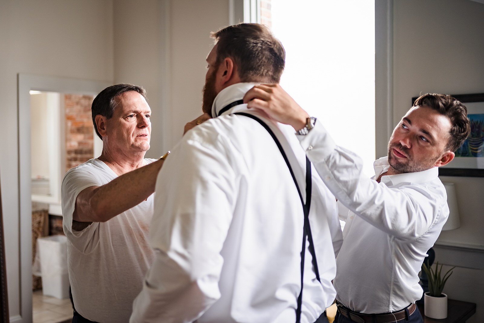 Groom's father and friend help him with his bow tie