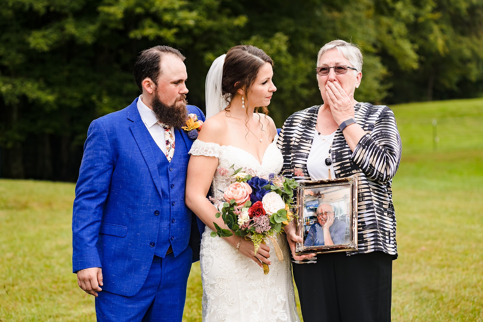 Bride and groom pose with bride's grandmother who reacts emotionally to holding a photograph of her recently deceased husband