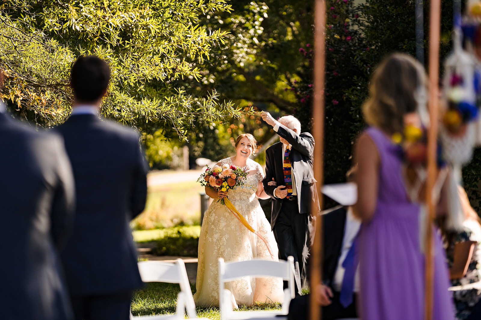 Father of the bride moves a branch out of the way as he walks his daughter down the aisle