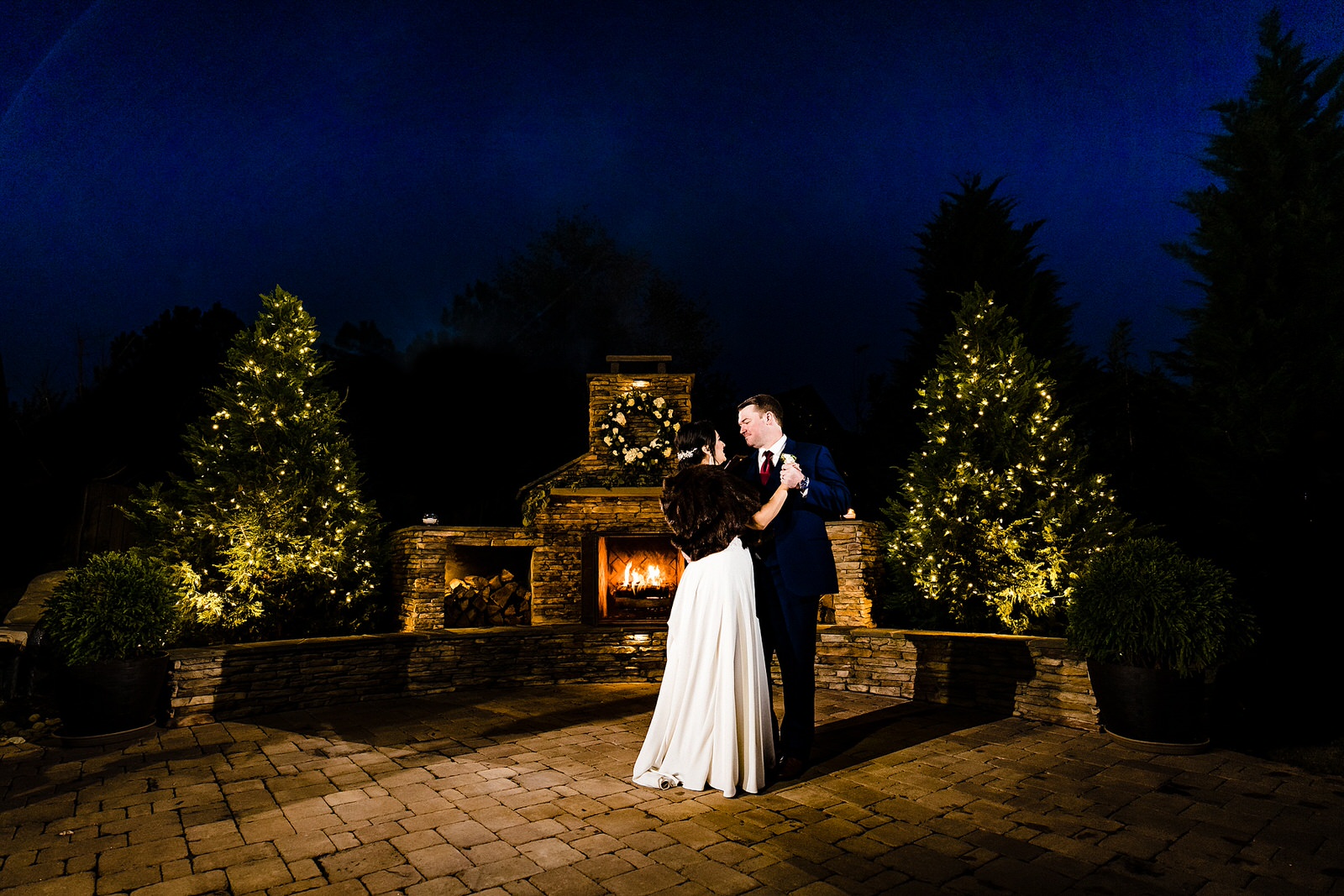 bride and groom have their first dance in front of an outdoor fireplace at a backyard winter wedding