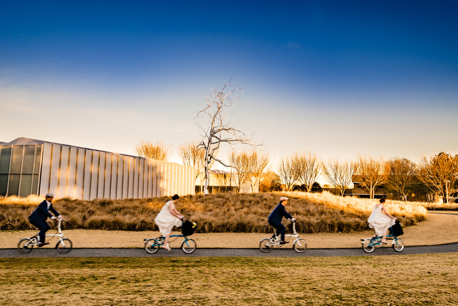 bride and groom ride through the North Carolina Museum of Art on their bicycles after their winter elopement